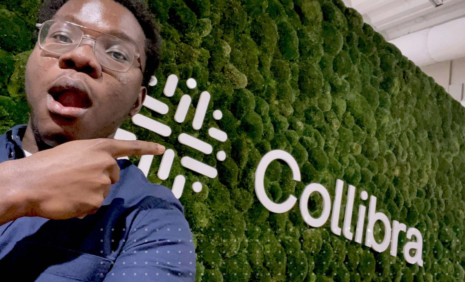 亚愽视频Collibra实习生Sam Mensah用他的手指指着带有Collibra大标志的生活墙。