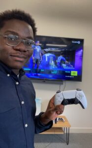 Sam Mensah在电视屏幕前拿着一个视频游戏控制器，屏幕上显示着视频游戏FIFA22。